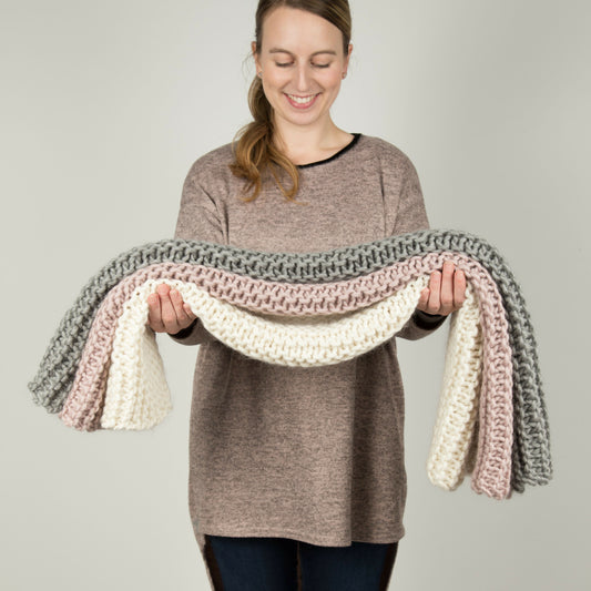 Woman holding a colorful knitted scarf against a plain background