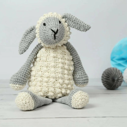 Knitted toy sheep on a light wooden surface with a neutral background
