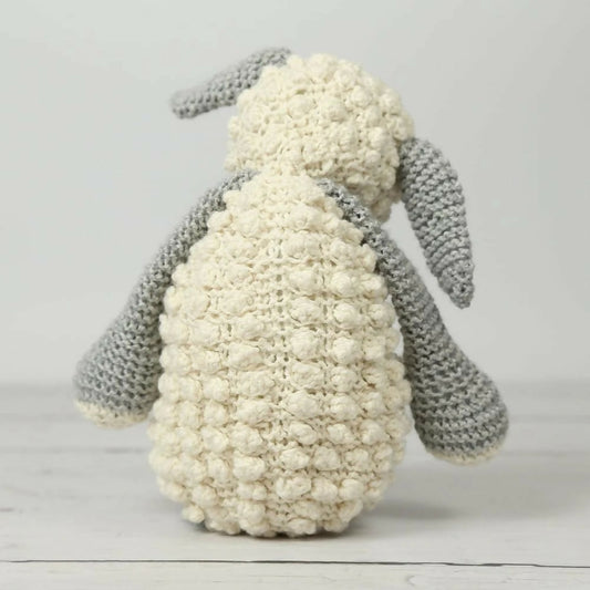 Knitted toy lamb with white body and gray arms on a light wooden surface