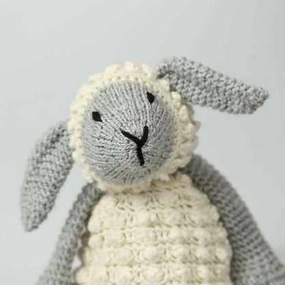 Knitted toy sheep with gray body and white wool on a light gray background