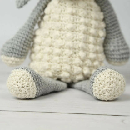 Knitted lamb toy with white body and gray ears on a light wooden surface