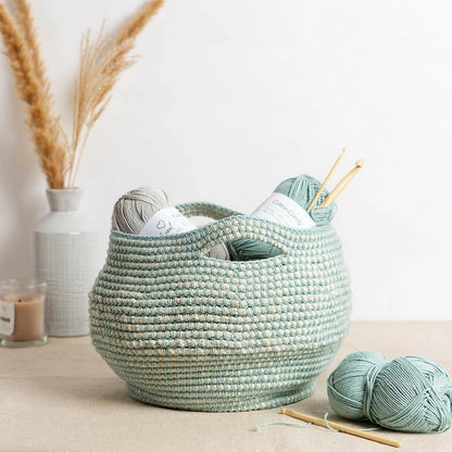 Woven basket with yarn and knitting needles on a light surface, with decorative elements in the background.