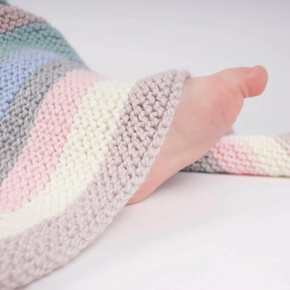 Pastel striped knitted blanket with a hand peeking out from under it on a white background
