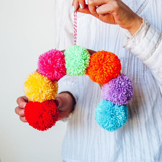 Colorful pom-pom decorations held by a person against a white background