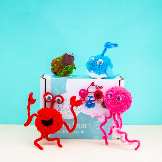 Colorful pom-pom monsters in front of a blue background with a box labeled 'Pom Pom Friends'.