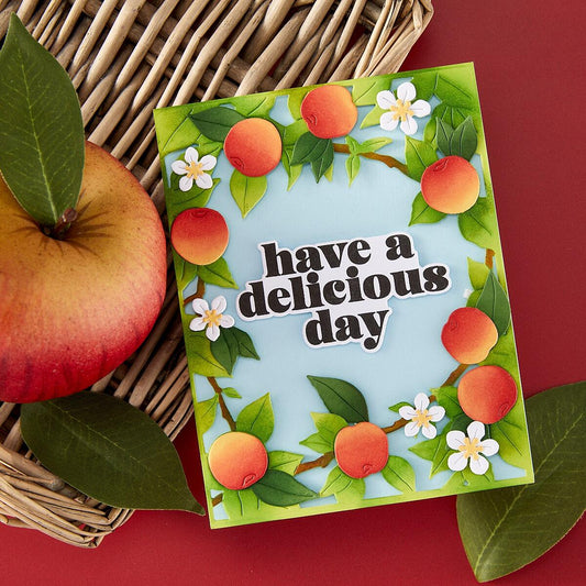 Card with apples and flowers and 'have a delicious day' text, next to an apple on a red background.