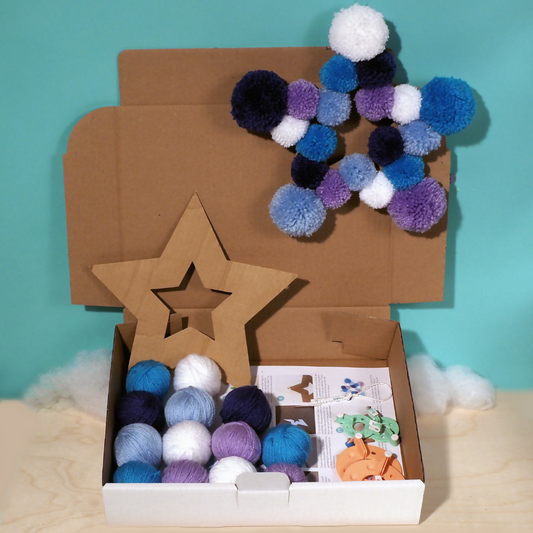 Cardboard box with star-shaped pom-pom wreath and craft materials on a teal background