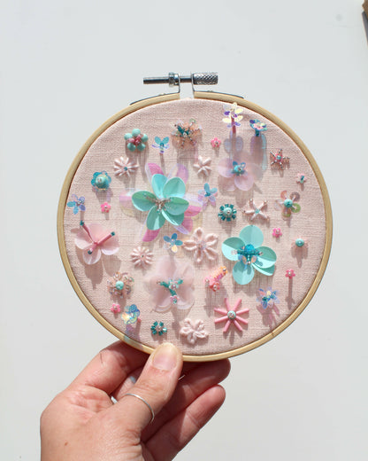 Hand holding an embroidery hoop with floral and butterfly design on a light background