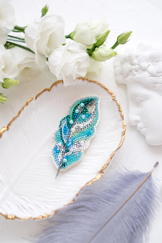 Blue feather brooch on a decorative plate with flowers and feathers