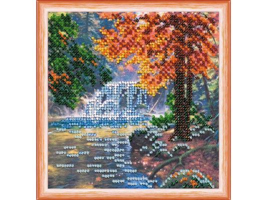 Embroided scene with autumn tree, bridge, and water body.