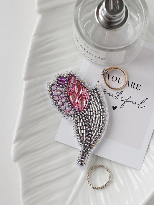 Decorative brooch with pink gemstones on a white surface with a perfume bottle and card.