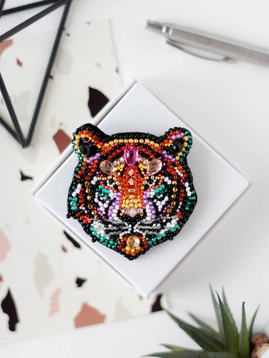 Colorful beaded tiger head on a white card with geometric shapes and a pen in the background