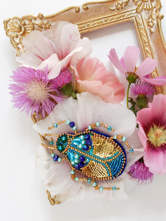 Decorative brooch with beads and flowers in front of a gold frame