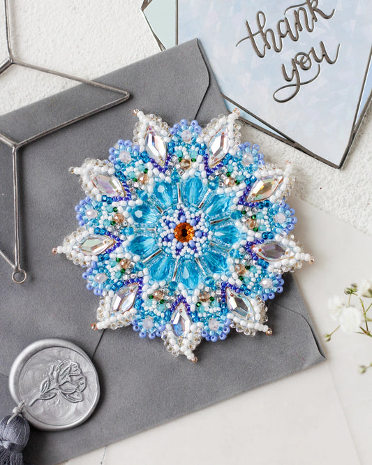 Decorative brooch with blue gemstones on a gray surface with 'thank you' card in the background